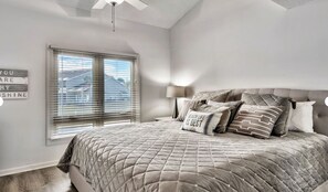 Een slaapkamer met een groot bed, een raam met zonwering, een plafondventilator en een bord aan de muur.