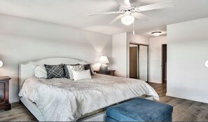 Une chambre à coucher avec un lit, une table de chevet, une lampe, un ventilateur de plafond et une porte.