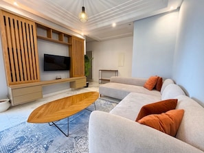 Un salon moderne avec un canapé d’angle, une table basse, un téléviseur et des étagères intégrées.