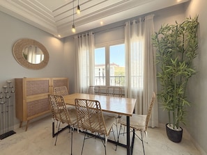 Un coin repas avec une table en bois et des chaises en osier, un miroir et une plante en pot.
