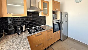 Eine moderne Küche mit Holzausstattung, einer schwarzen Fliesenspiegel und Edelstahlgeräten. Auf der Wand hängt eine Uhr.