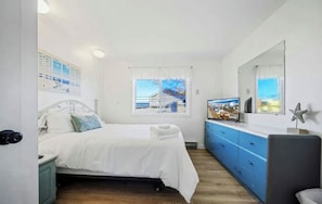 A bedroom with a bed, a dresser, a mirror, and a window with a view.