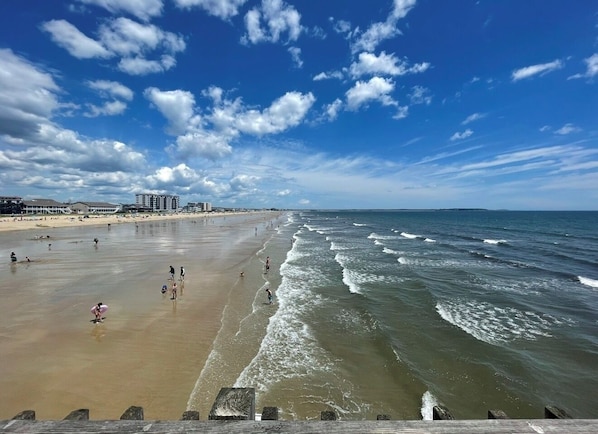 A beach with people, waves, and buildings in the background.