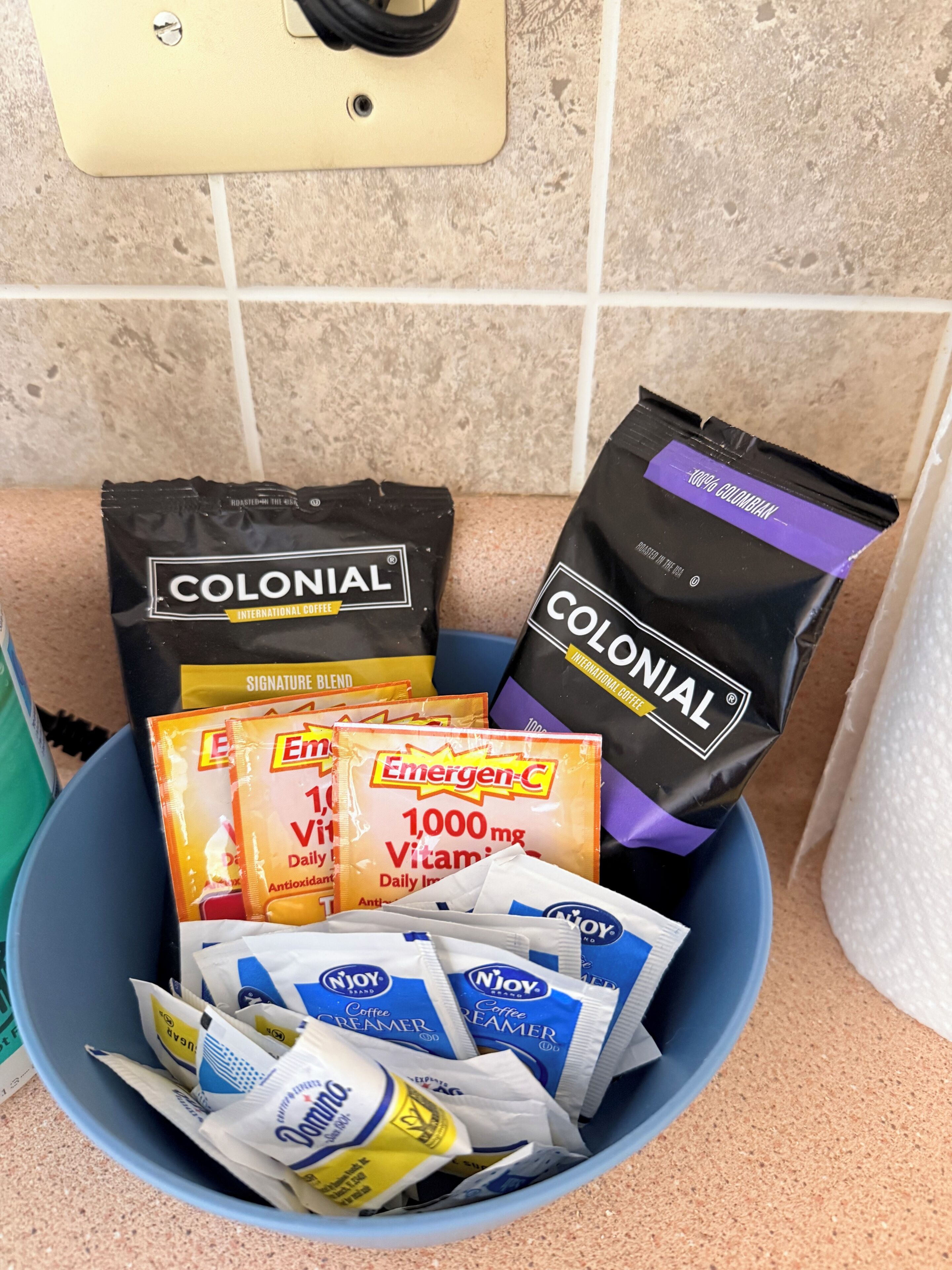 Un cuenco azul con varios sobres de leche para café y bolsas de café.
