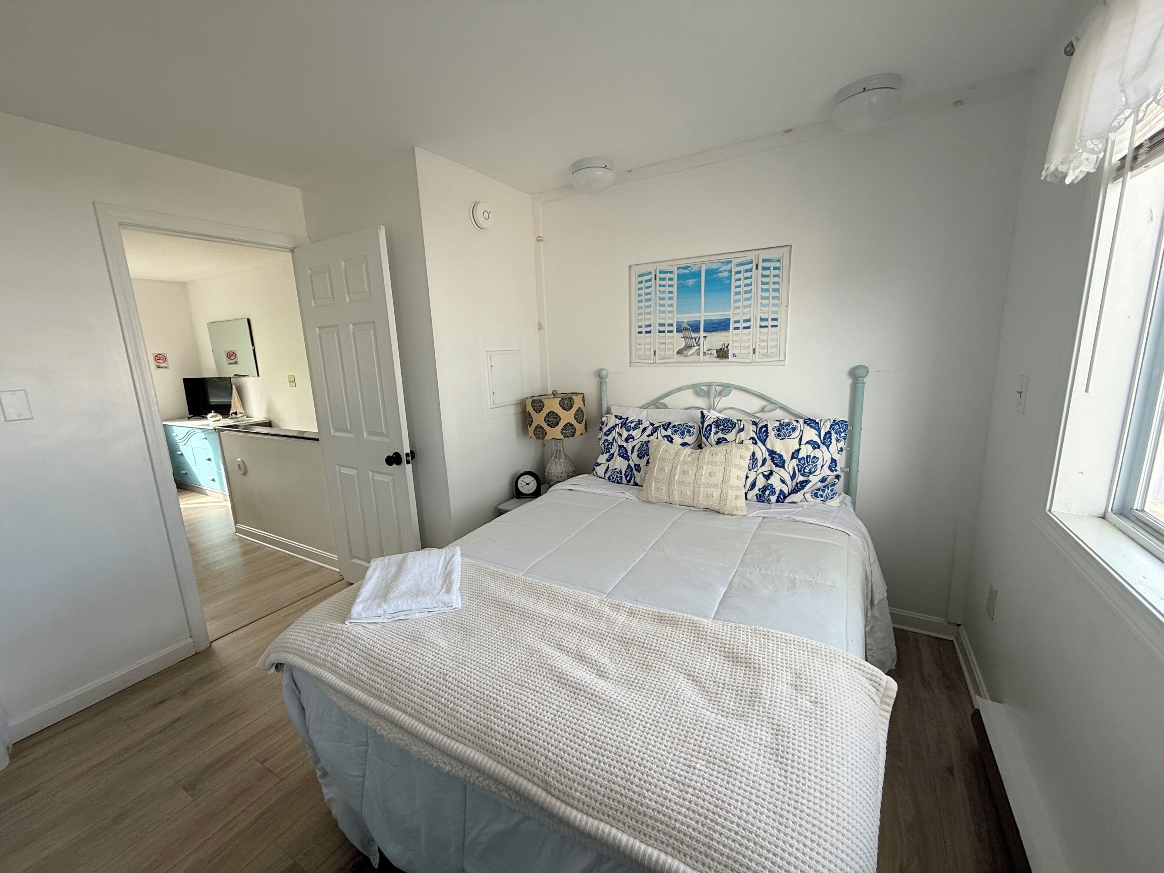A bedroom with a bed, a bedside table, a lamp, a clock, and a window with a view of the sea.