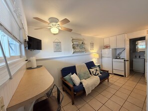 A kitchen with a ceiling fan, a dining table with chairs, a blue sofa with cushions, and a refrigerator.