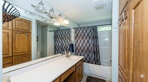 Ein Badezimmer mit einem großen Spiegel, Holzschränken, einem weißen Waschbecken und einer Dusche mit gemusterten Vorhängen.