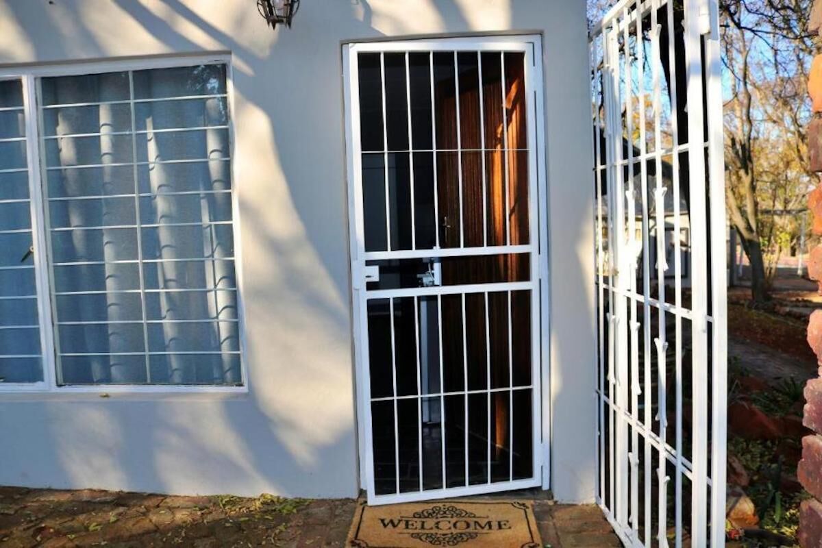 A white house with a barred door, a window with blinds, and a welcome mat.