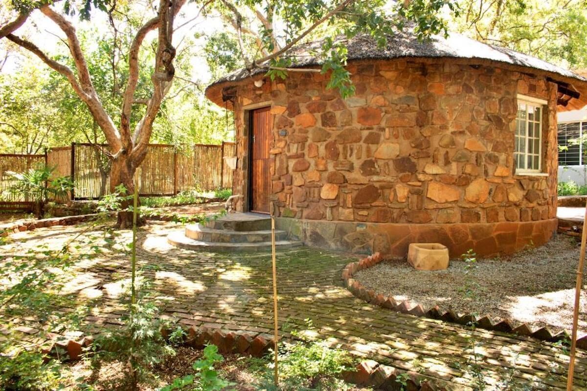 A stone cottage with a thatched roof, surrounded by a garden with a brick pathway and a wooden fence.