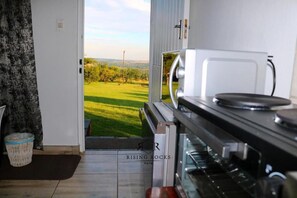 A kitchen with a view of a green field, a white door, and a basket on the floor.