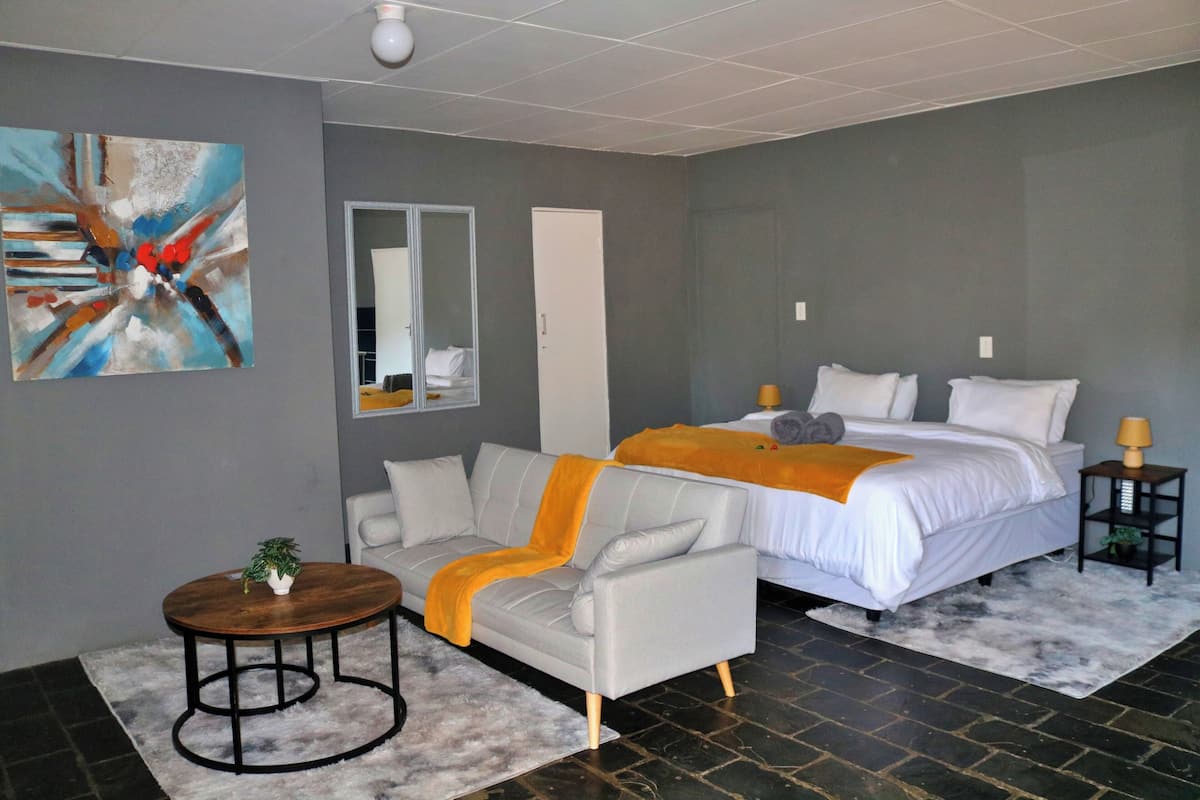 A modern bedroom with a bed, a sofa, a small table, and a painting on the wall.