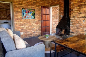 A cozy living area with a brick wall, a wooden table, a sofa, and a fireplace.
