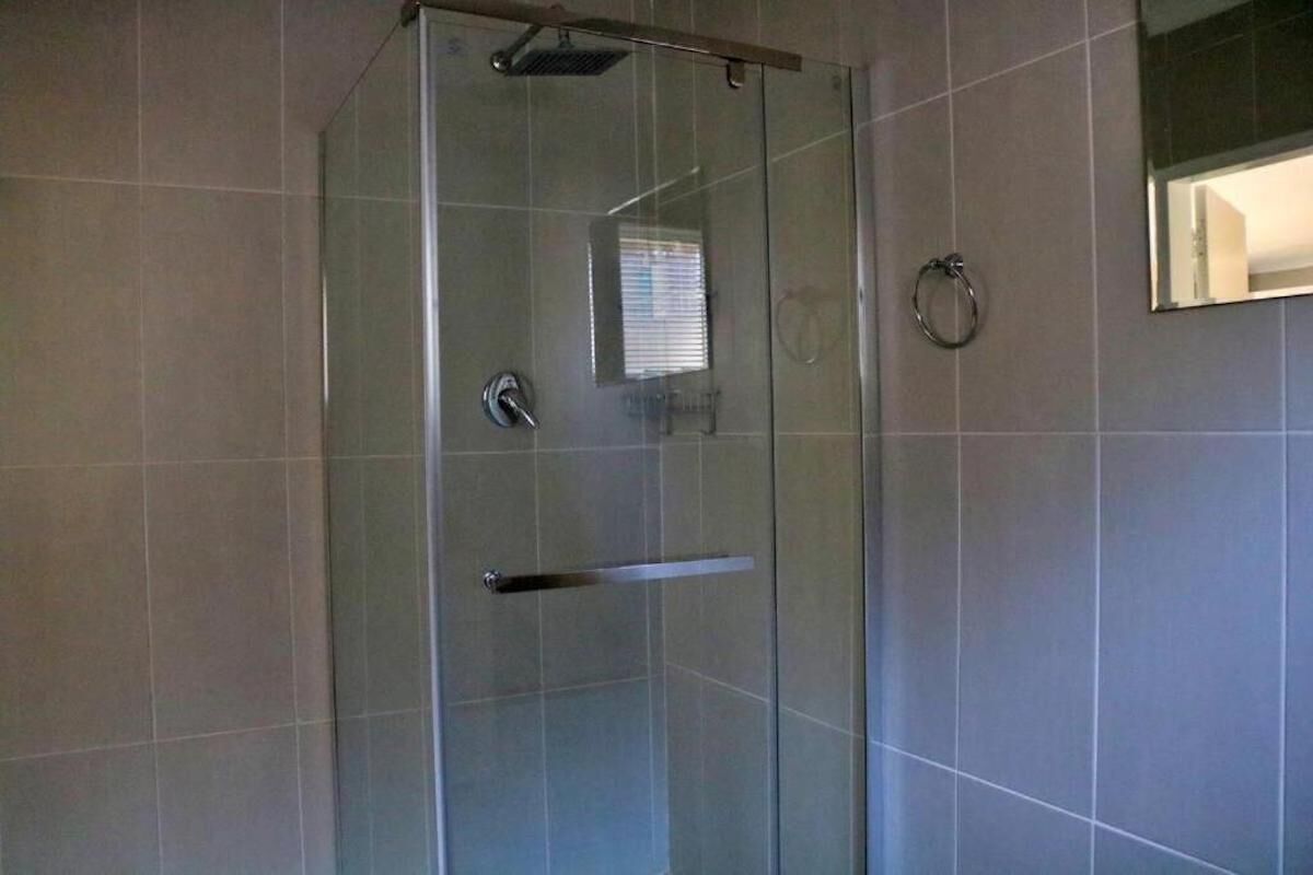 Cabina de ducha con paredes de vidrio, un cabezal de ducha de mano, un perchero y un espejo en la pared.