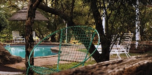A pool area with a netted swing chair, lounge chairs, and a thatched umbrella. - Rising Rocks Farm (Magaliesburg)
