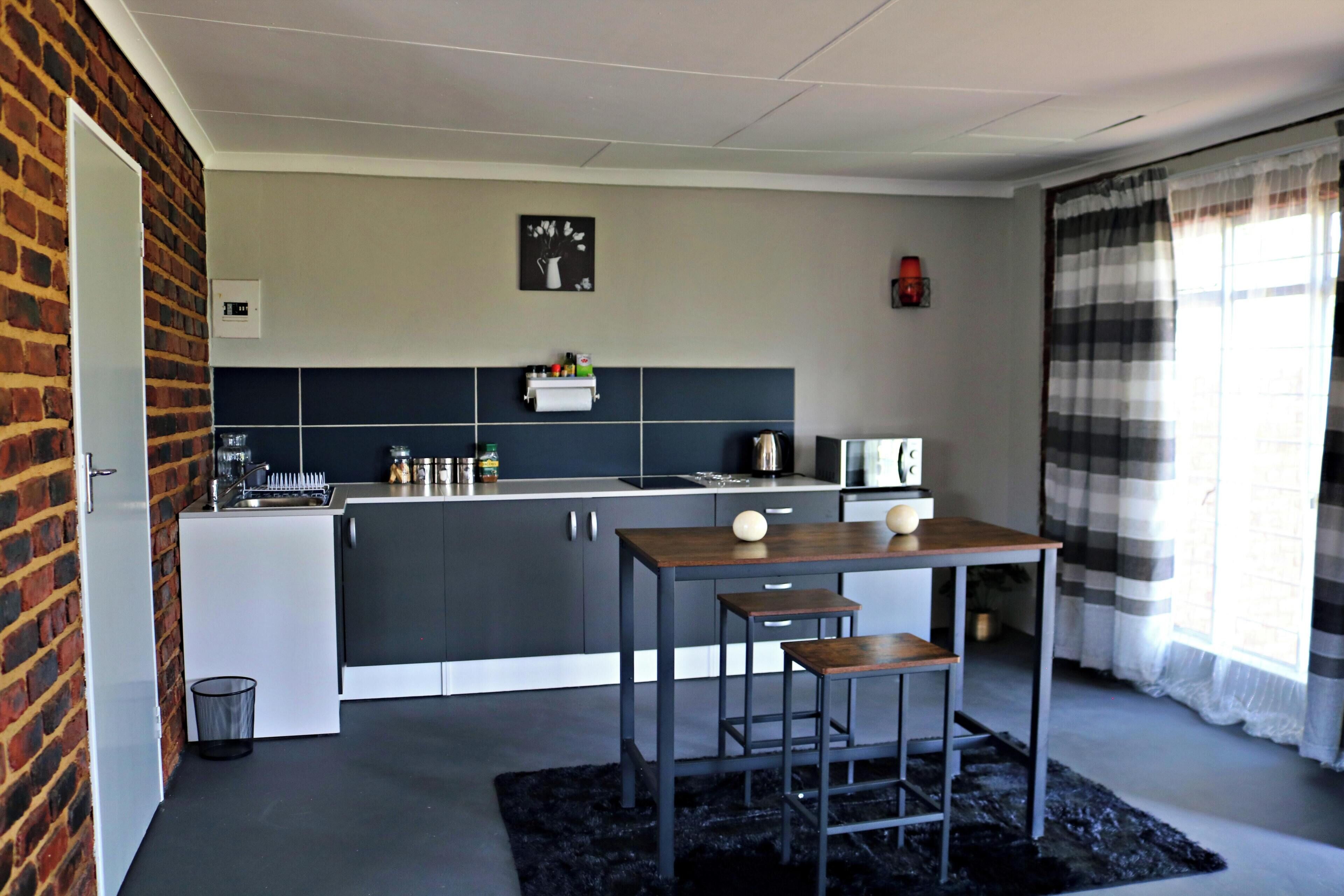 A modern kitchen with a central island, bar stools, and a black rug.