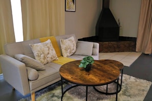 A living room with a sofa, a round coffee table, a fireplace, and a rug. - Rising Rocks Farm (Magaliesburg)