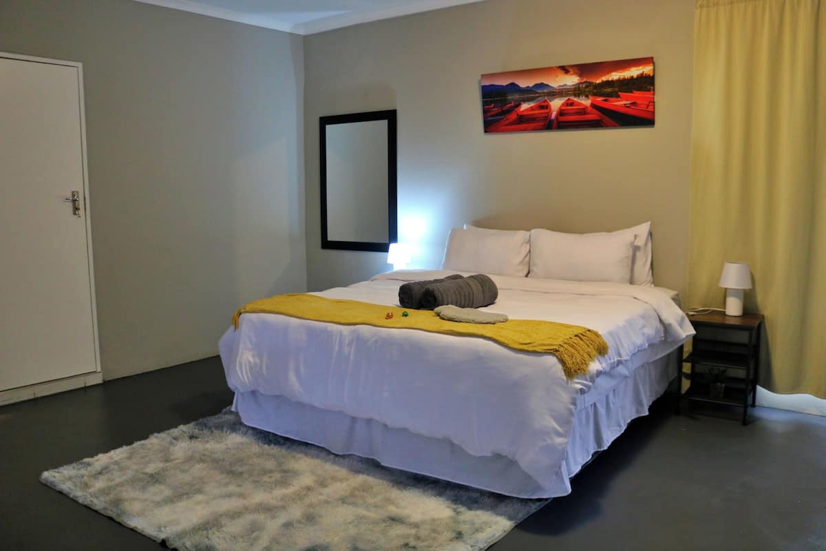 A hotel room with a bed, a nightstand, a lamp, a painting on the wall, and a door.