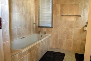 A bathroom with a bathtub, a window with blinds, a towel rack, and a black rug. - Rising Rocks Farm (Magaliesburg)