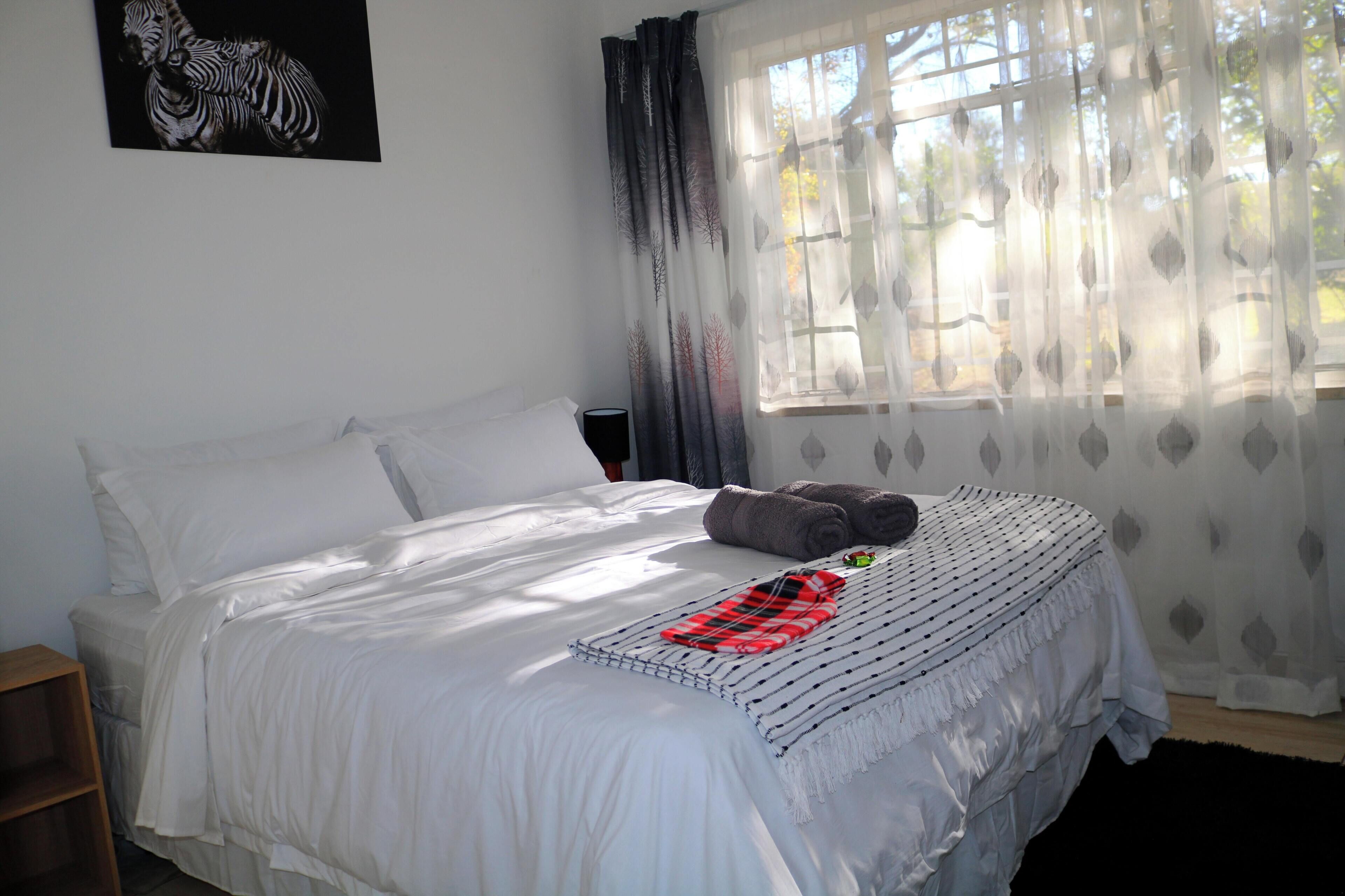 A neatly made bed with white linens, a red and black striped blanket, and a pillow. There is a wooden nightstand beside the bed.