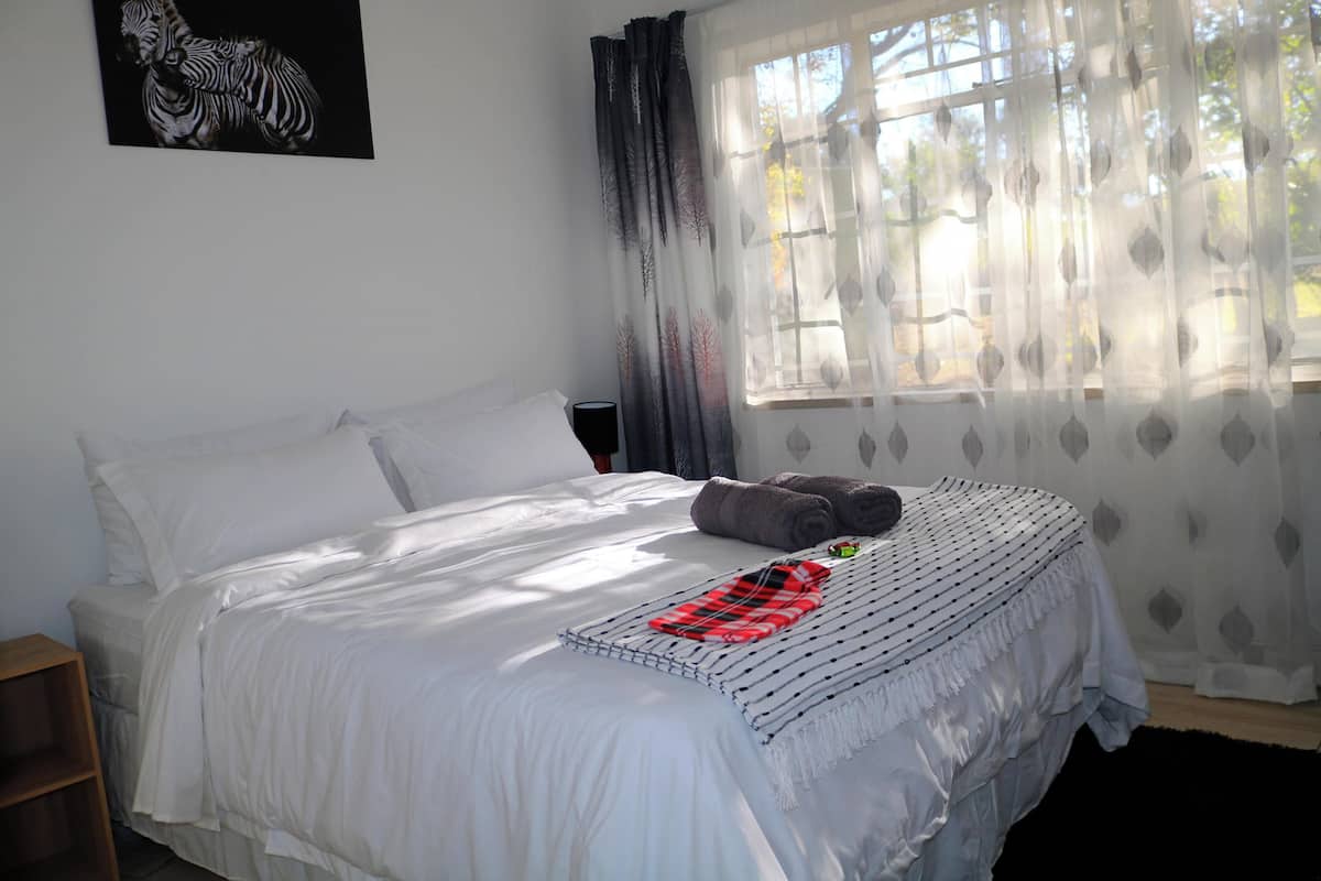 A neatly made bed with white linens, a red and black striped blanket, and a pillow. There is a wooden nightstand beside the bed.