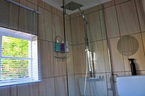 A shower with a glass enclosure, a window with blinds, and a toilet with a circular mirror. - Rising Rocks Farm (Magaliesburg)