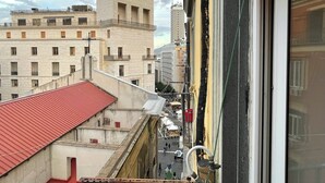 Ein mehrstöckiges Gebäude mit rotem Dach, einem Balkon und Blick auf eine Straße mit weiteren Gebäuden.