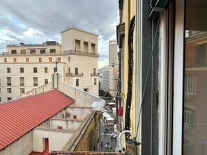Ein mehrstöckiges Gebäude mit rotem Dach, einem Balkon und Blick auf eine Straße mit weiteren Gebäuden.