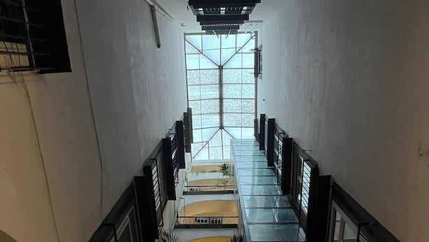 Ein mehrgeschossiges Interieur mit Glasgeländern, einer zentralen Treppe und Pflanzen in Kübeln auf Balkonen.