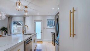 Una cucina moderna con mobili bianchi, maniglie dorate, un frigorifero in acciaio inossidabile e un forno integrato.