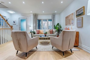 Un salon comprenant un canapé, deux fauteuils, une table basse et un escalier.