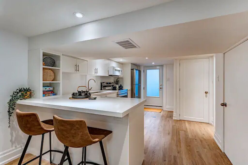 A modern kitchen with white cabinetry, a central island with bar stools, and a view to a room with a door.