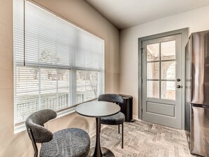 Ein kleiner Raum mit einem runden Tisch und zwei Stühlen, einer Tür mit Fenster sowie einem Kühlschrank.
