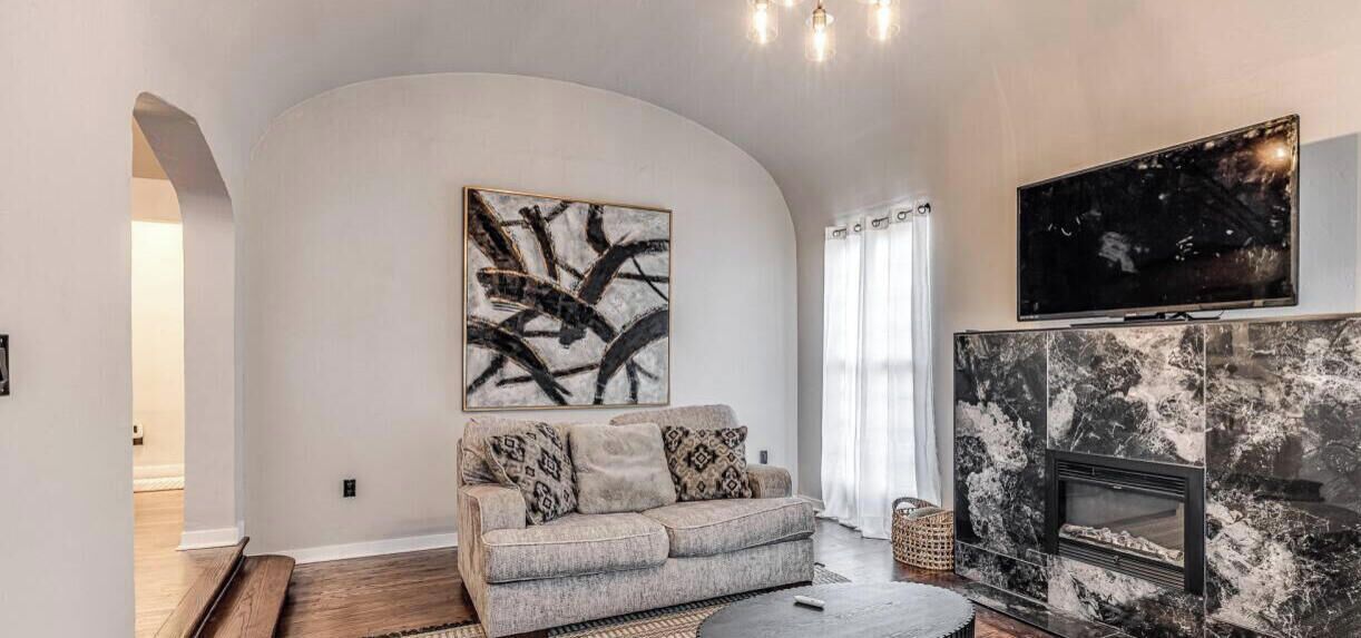 Un salon avec un canapé, une cheminée, un téléviseur et un grand tableau abstrait.