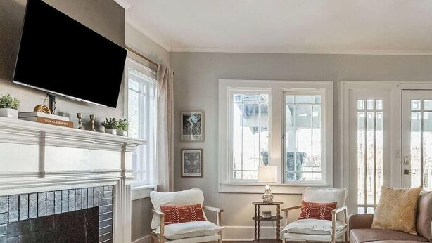 Un salon avec une cheminée, deux fauteuils, un canapé, une télévision et de grandes fenêtres.