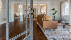 Un salon spacieux avec une grande fenêtre, un canapé et un coin repas à l’arrière-plan.