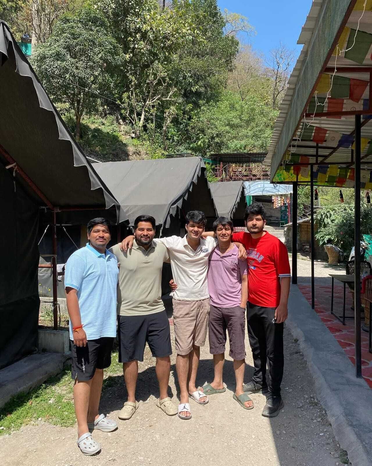 A group of people standing in front of a building with a corrugated metal roof and a small overhang.