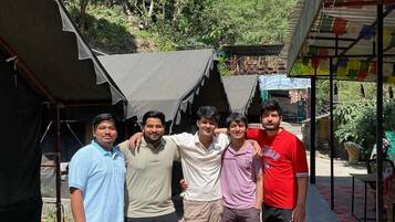 A group of people standing in front of a building with a corrugated metal roof and a small overhang.
