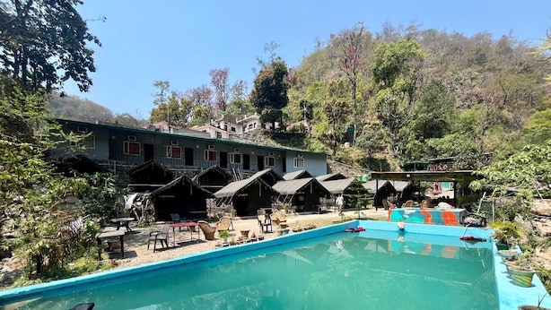 A pool area with lounge chairs, a swimming pool, and several small huts. - Weekend Getaway Camps (Tapovan)
