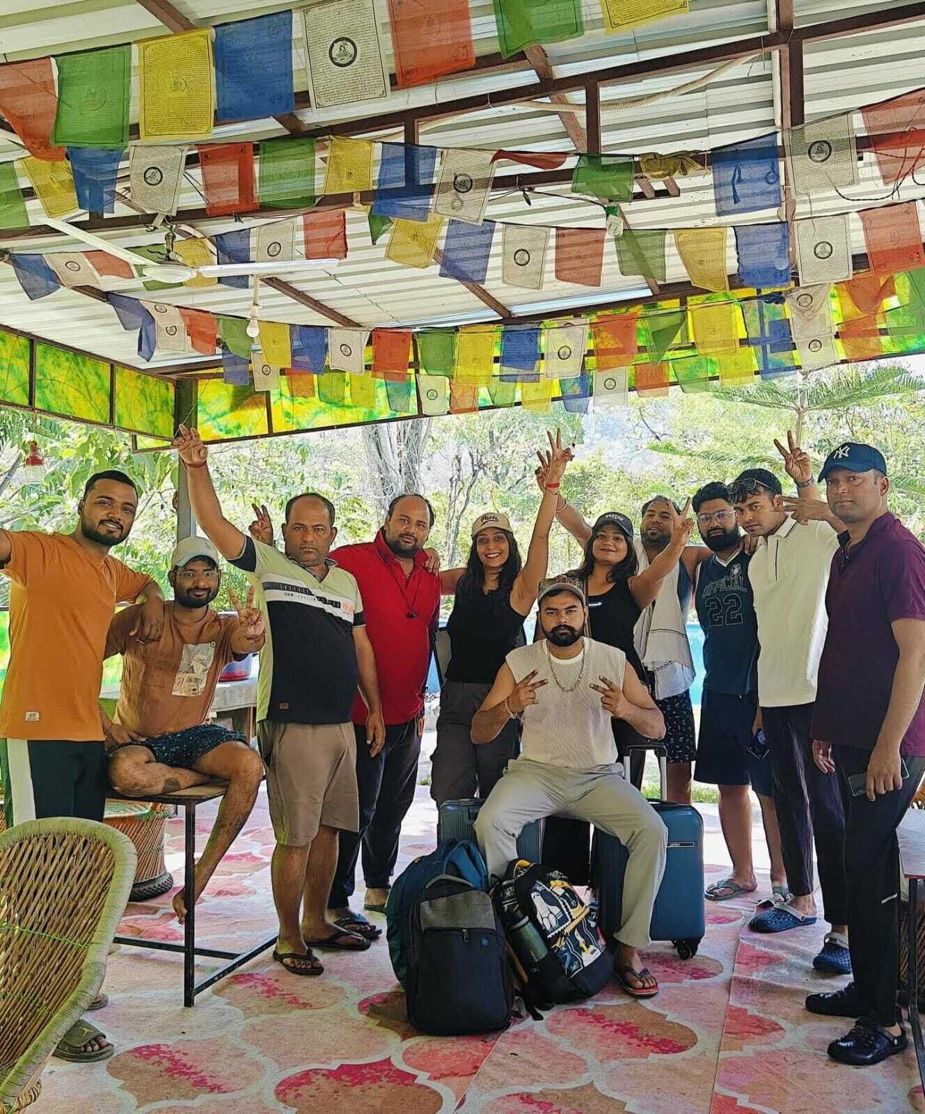A group of people in a covered outdoor area with colorful prayer flags hanging above.