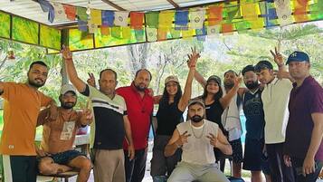 A group of people in a covered outdoor area with colorful prayer flags hanging above.