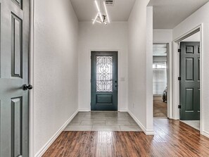 Ein Flur mit Holzboden, einer dunklen Tür mit dekorativer Glasverkleidung und einer Deckenleuchte.