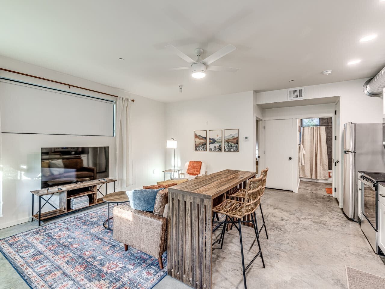 A modern kitchen with a built-in oven, a dining area with a wooden table and chairs, and a TV mounted on the wall.