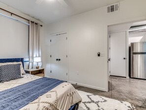 Ein Schlafzimmer mit Bett, Nachttisch, Kleiderschrank und einer Küchenzeile mit Kühlschrank.
