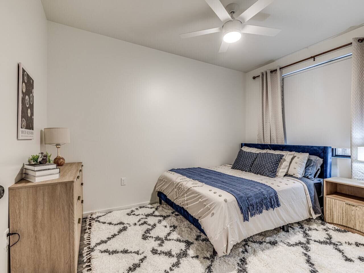 A bedroom with a bed, a ceiling fan, a dresser, and a rug.