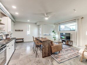 A modern kitchen with a dining area, a TV, and a large window.