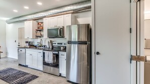 A modern kitchen with stainless steel appliances, white cabinetry, and a visible ductwork system. - Midtown OKC 1Bed Hideaway (Oklahoma City)