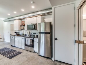 Una cocina moderna con electrodomésticos de acero inoxidable, armarios blancos y un sistema de conductos visible.