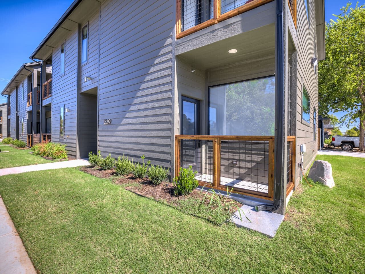 A modern two-story building with a well-maintained lawn, a covered outdoor seating area, and a visible garage.
