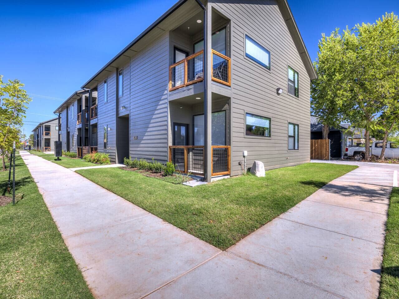 A modern multi-story residential building with a flat roof, large windows, and a well-maintained lawn.