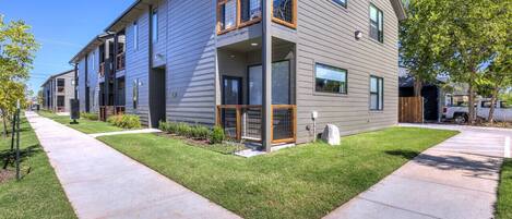 A modern multi-story residential building with a flat roof, large windows, and a well-maintained lawn.